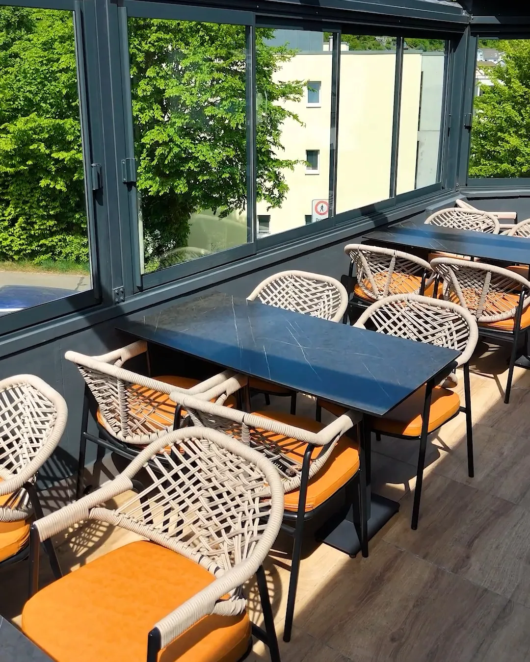 Verglaste Terrasse: Tische und Flechtstühle